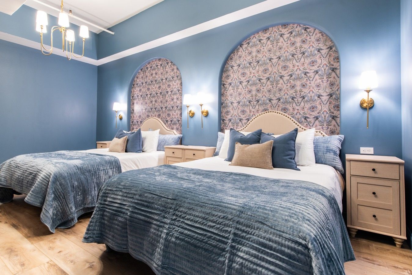 Une chambre avec deux lits, un lustre et un papier peint à motifs.