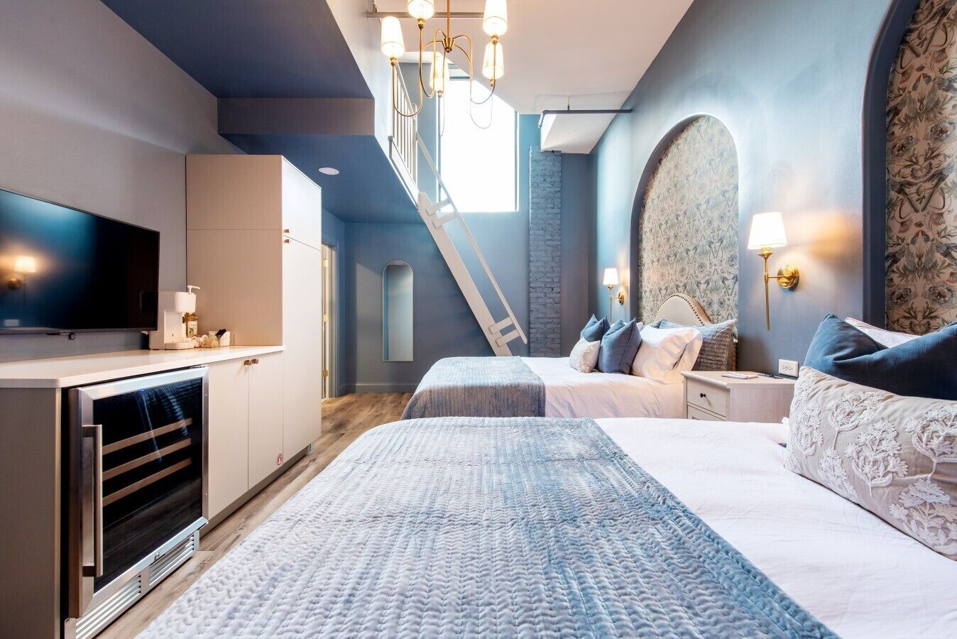 A modern bedroom with a large bed, a television, and a staircase leading to an upper level.