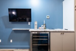 A bathroom with a blue wall, a mounted TV, a sink with toiletries, and a cabinet. - Hollyhock Suite 306: 1 bed + 1 loft bed/1 bath (Louisville)