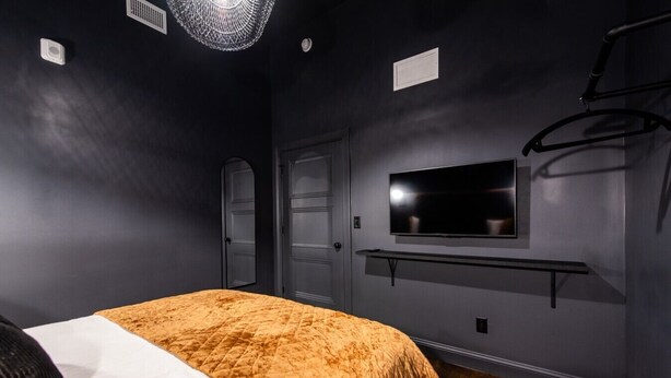 Une chambre à coucher avec un lit, un téléviseur fixé au mur et un luminaire au plafond.