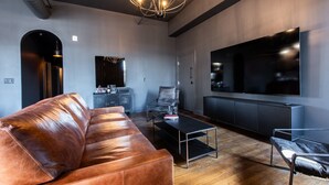 Un salon moderne avec un canapé en cuir, une table basse, un téléviseur et un lustre.