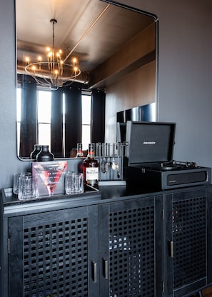 A bar area with a mirror, a chandelier, and a speaker. There are glasses, bottles, and a book on the counter. - Hollyhock Suite 502: 4 bed/2 bath with soaking tub (Louisville)