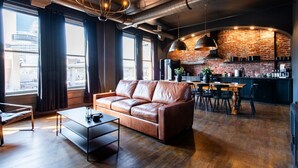 Un salon moderne avec un canapé en cuir, une table à manger et un coin cuisine doté de murs en briques apparentes et d’un éclairage de style industriel.