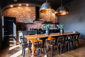 A modern kitchen with a brick wall, stainless steel appliances, and a wooden dining table with chairs. - Hollyhock Suite 502: 4 bed/2 bath with soaking tub (Louisville)