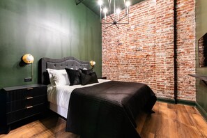 Ein Schlafzimmer mit Backsteinwand, einem Bett mit schwarzer Bettwäsche, einem Nachttisch und einer modernen Leuchte.