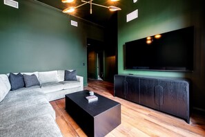 Ein modernes Wohnzimmer mit einem Ecksofa, einem schwarzen Couchtisch, Holzboden und einem großen Flachbildfernseher an der Wand.