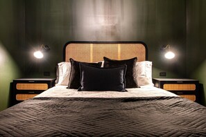 A neatly made bed with a geometric patterned bedspread, flanked by two nightstands with woven side tables and wall-mounted lamps. - Hollyhock Suite 305: 2 beds/1 bath (Louisville)