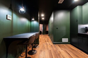 A modern interior with a long table and chairs, a kitchen area, and a brick wall in the background. - Hollyhock Suite 305: 2 beds/1 bath (Louisville)