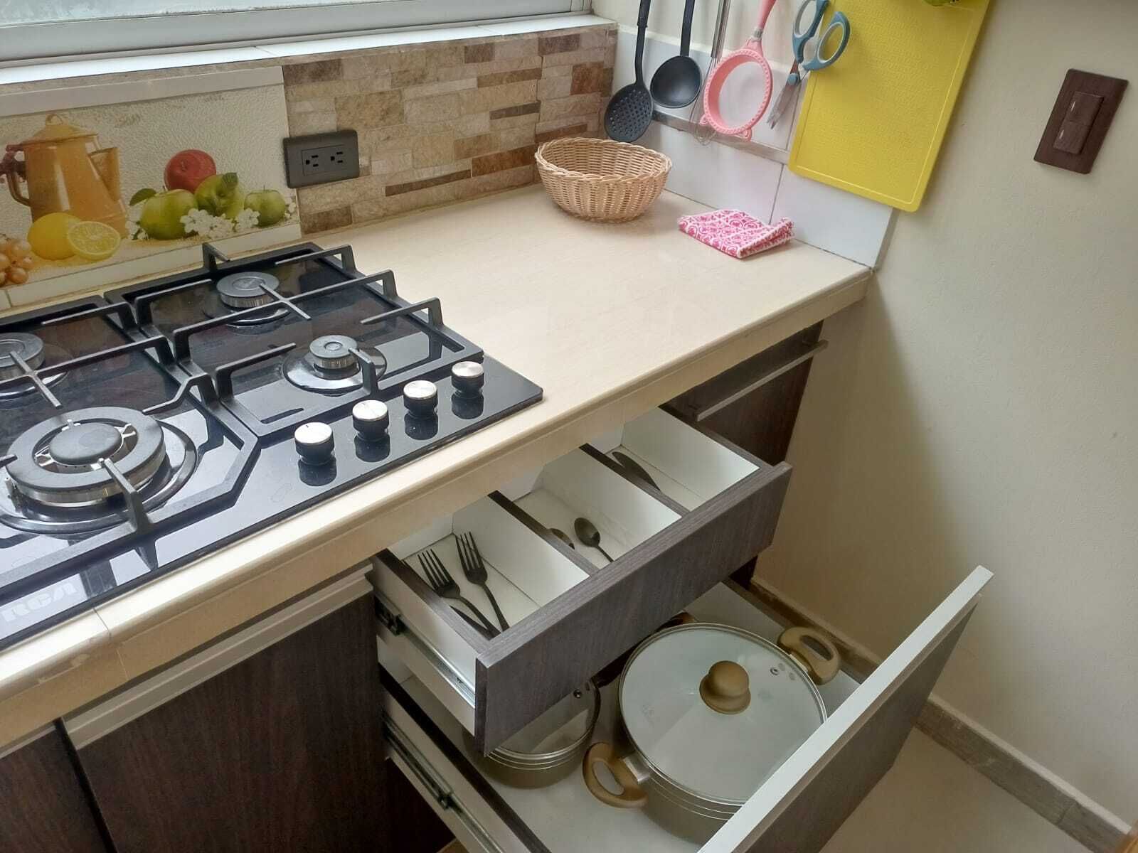 A kitchen with a gas stove, a drawer with utensils, a basket, and a wall-mounted basket holder.