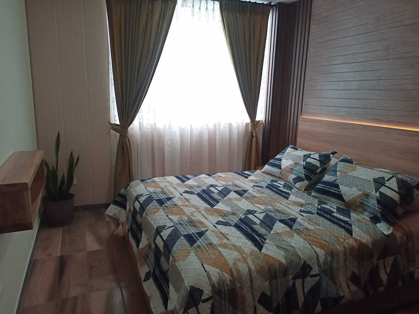Un dormitorio con cama, cortinas, una planta en maceta y un cabecero de madera.