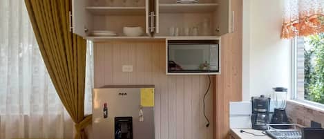 Cocina compacta con microondas integrado, un refrigerador y ventana con vista a follaje.
