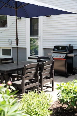 Eine Terrasse im Freien mit Tisch und Stühlen, einem Grill und einem blauen Sonnenschirm.