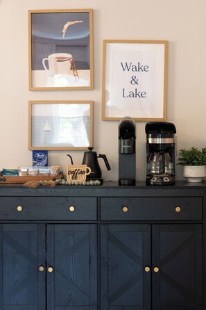 A kitchen counter with coffee-making equipment, framed artwork, and a coffee mug. - Walk to Lake & Restaurants | Fire Table, Ping Pong, Shuffleboard | Sleeps 12 (Williams Bay)