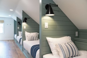 A bedroom with a sloped ceiling, two beds with white bedding, a striped pillow, and a black wall-mounted lamp.