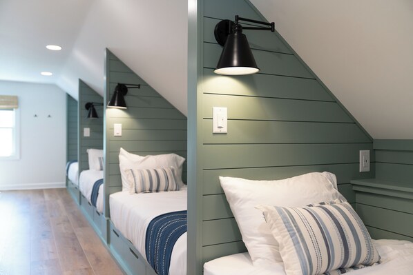 A bedroom with a sloped ceiling, two beds with white bedding, a striped pillow, and a black wall-mounted lamp. - Fall Getaway with Gas Fire Table | Walk to Lake, Restaurants | Sleeps 12 (Williams Bay)