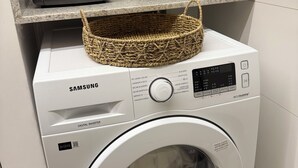 Eine Samsung Digital Inverter Waschmaschine mit einem Korb obenauf, eine Kaffeemaschine und ein Wasserfilter auf der Arbeitsplatte.