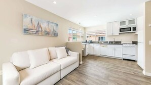 A modern living room with a beige sofa and a painting of sailboats on the wall. - Del Mar Studio - Walk to Beach (Del Mar)