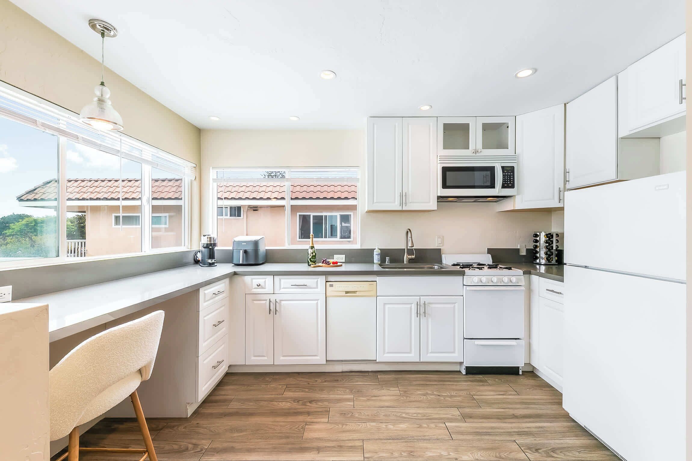 Een moderne keuken met witte kasten, een ingebouwde magnetron, een fornuis en een vaatwasser.