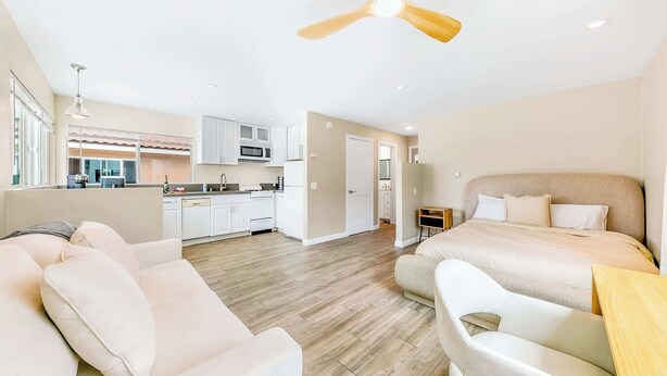 A modern hotel room with a bed, a sofa, a small table, and a kitchenette in the background. - Del Mar Studio - Walk to Beach (Del Mar)