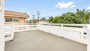 A residential property with a fenced patio, a house with a tiled roof, and a lush green tree in the background. - Del Mar Studio - Walk to Beach (Del Mar)