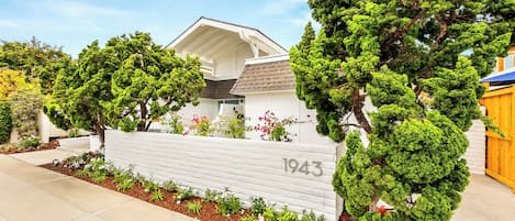 Una propiedad residencial con fachada blanca, el número '1943' en la pared, y un jardín cuidado con diversas plantas y flores.