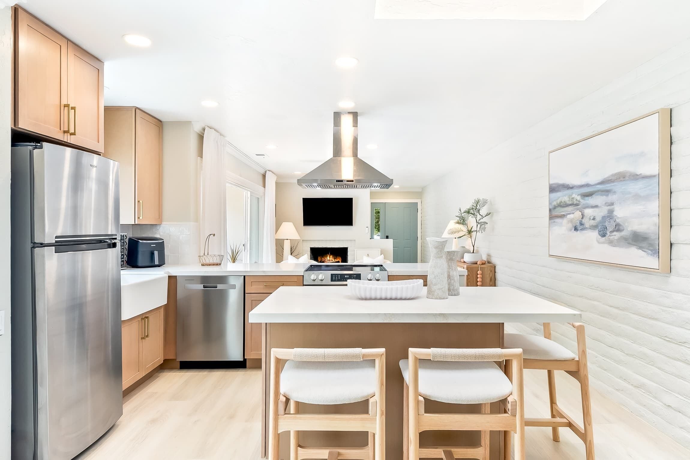 A modern kitchen with stainless steel appliances, a central island with seating, and a large painting on the wall.