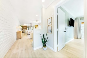 A modern interior with a wooden floor, white walls, a flat-screen TV mounted on the wall, and a potted plant. - Designer Del Mar Escape , Beach, Dining & Shops (Del Mar)