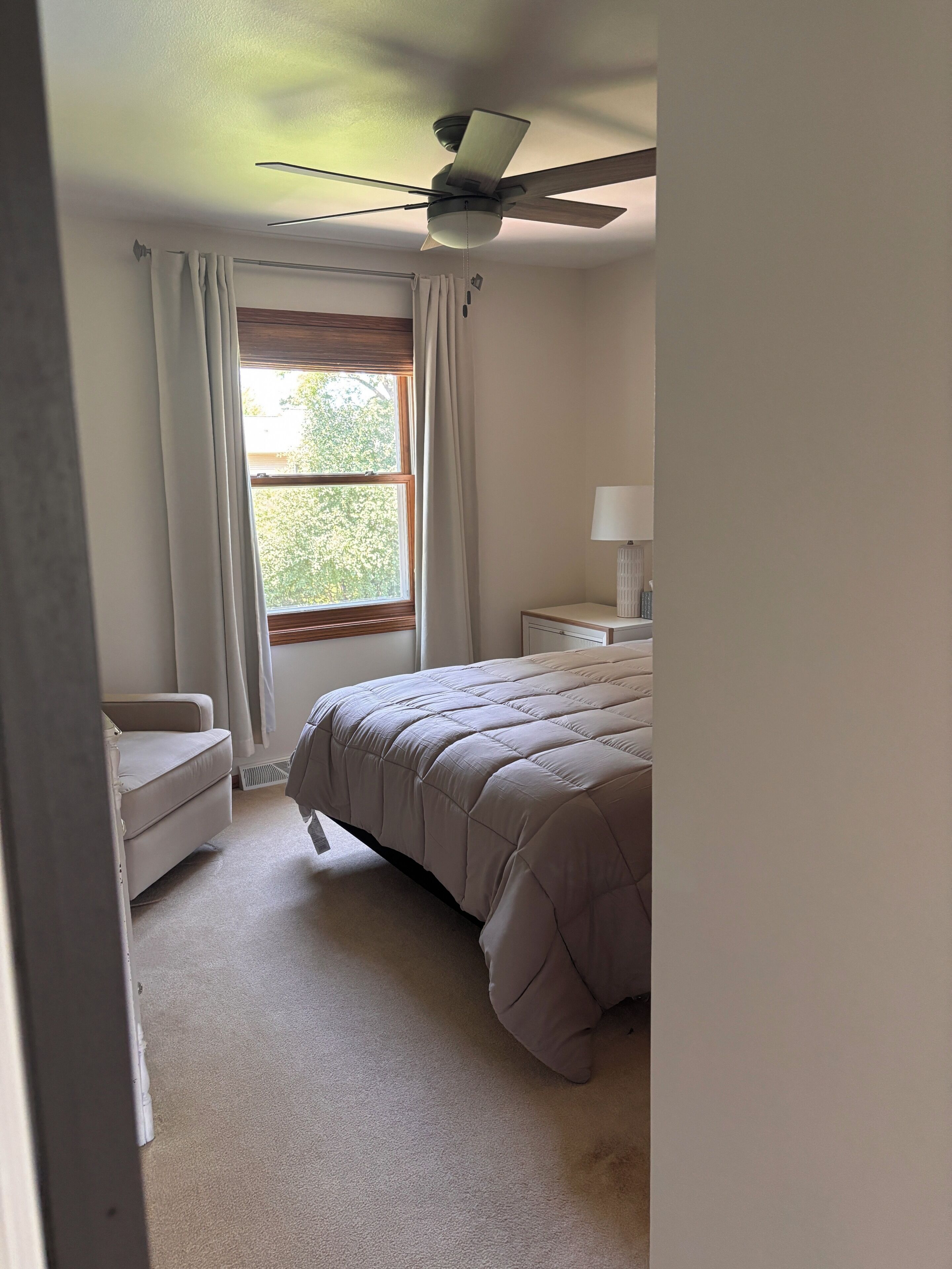 Ein Schlafzimmer mit Bett, Stuhl, Nachttisch, Lampe und Deckenventilator.