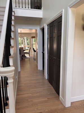A hallway with a wooden floor, a dark door, and a staircase with white balusters. - Spacious 4-bedroom home less than 5 miles away from EAA in Oshkosh with a gym (Oshkosh)