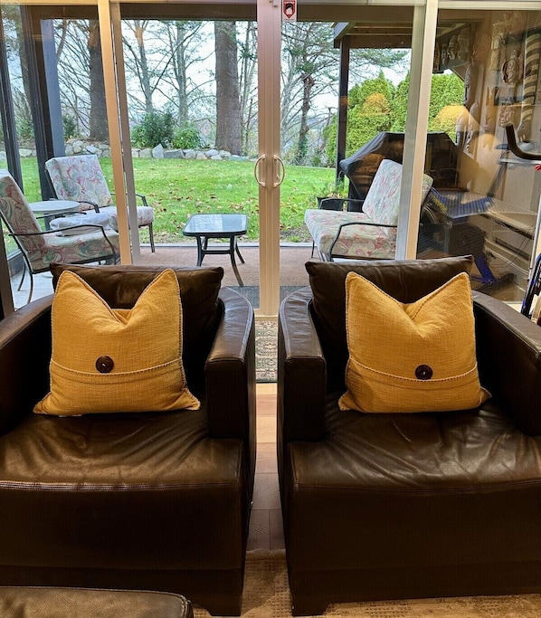 A room with two leather sofas facing a glass door leading to an outdoor patio area.