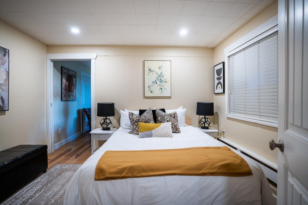 Un dormitorio con cama, mesitas de noche, una ventana con persianas y obras de arte en las paredes.