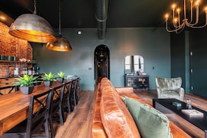 Un interior moderno con una mesa de comedor de madera, sillas, un sofá de cuero y una araña.