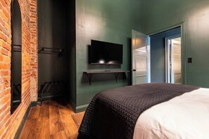 Una habitación de hotel con pared de ladrillo, televisor, cama con cubrecama acolchado y piso de madera.