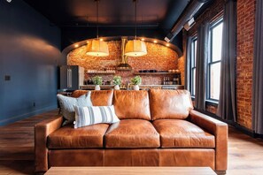 A modern living room with a leather sofa, a wooden coffee table, and a brick wall. - Hollyhock Suite 301: 4 Bed/2 Bath (Louisville)