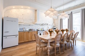 A modern kitchen with white appliances, wooden cabinets, and a dining area with a table set for six. - Hollyhock Suite 301: 4 Bed/2 Bath (Louisville)