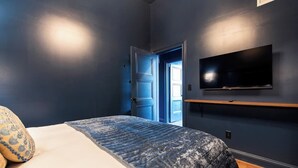 Ein Schlafzimmer mit einem Bett, einem an der Wand montierten Fernseher und einer Tür zu einem anderen Raum.