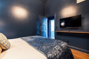 A bedroom with a bed, a TV mounted on the wall, and a door leading to another room. - Hollyhock Suite 301: 4 Bed/2 Bath (Louisville)