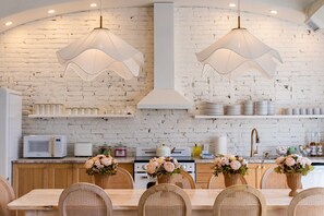 A modern kitchen with white brick walls, wooden cabinets, and a dining area with wicker chairs and a wooden table. - Hollyhock Suite 301: 4 Bed/2 Bath (Louisville)