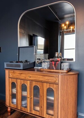A wooden cabinet with a mirror above it, a record player, and a bottle of Kentucky bourbon. - Hollyhock Suite 301: 4 Bed/2 Bath (Louisville)