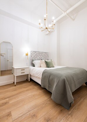 A bedroom with a bed, bedside table, nightstand, and a mirror. - Hollyhock Suite 301: 4 Bed/2 Bath (Louisville)