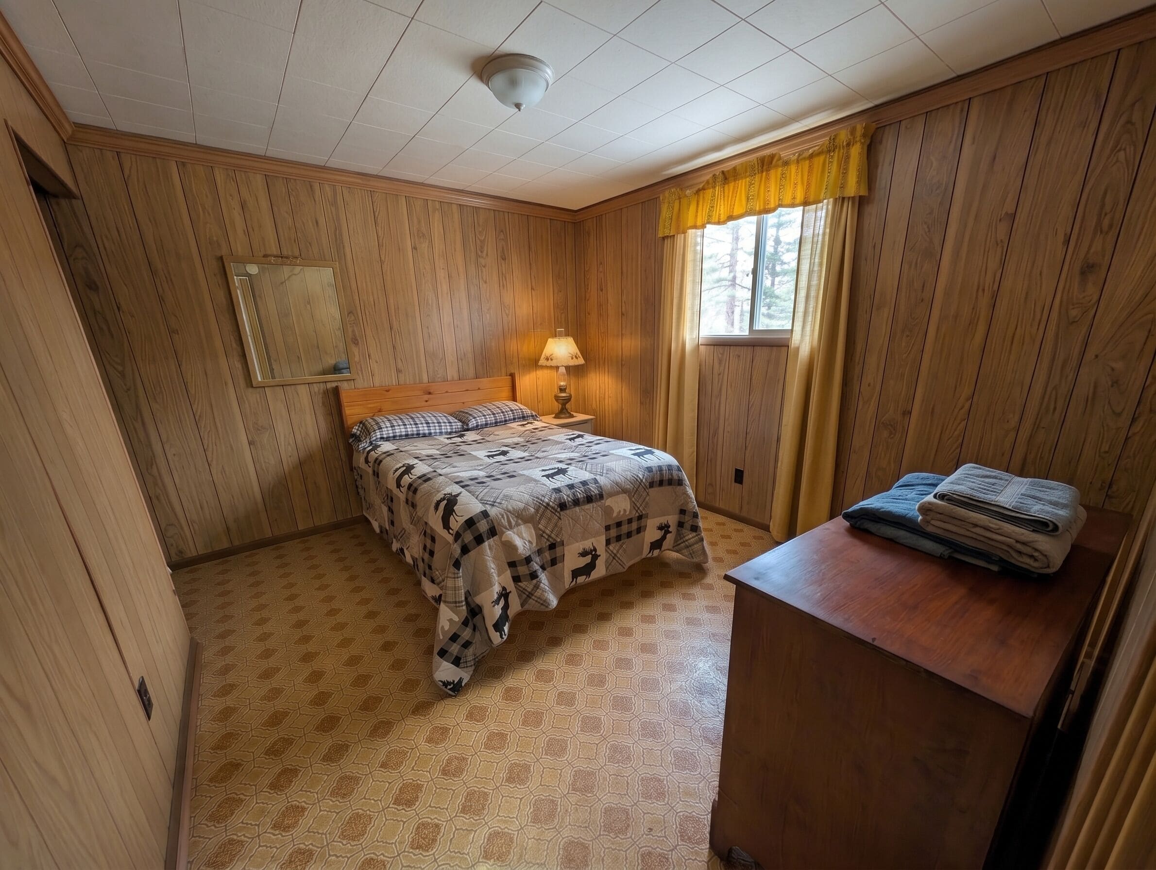 A room with a bed, a nightstand with a lamp, a mirror, and a window with curtains.