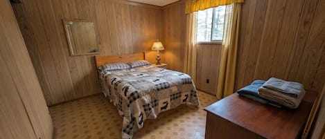 A room with a bed, a nightstand with a lamp, a mirror, and a window with curtains.