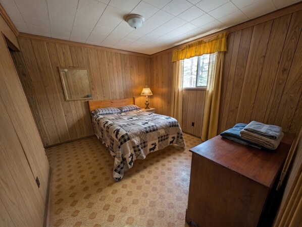 A room with a bed, a nightstand with a lamp, a mirror, and a window with curtains.