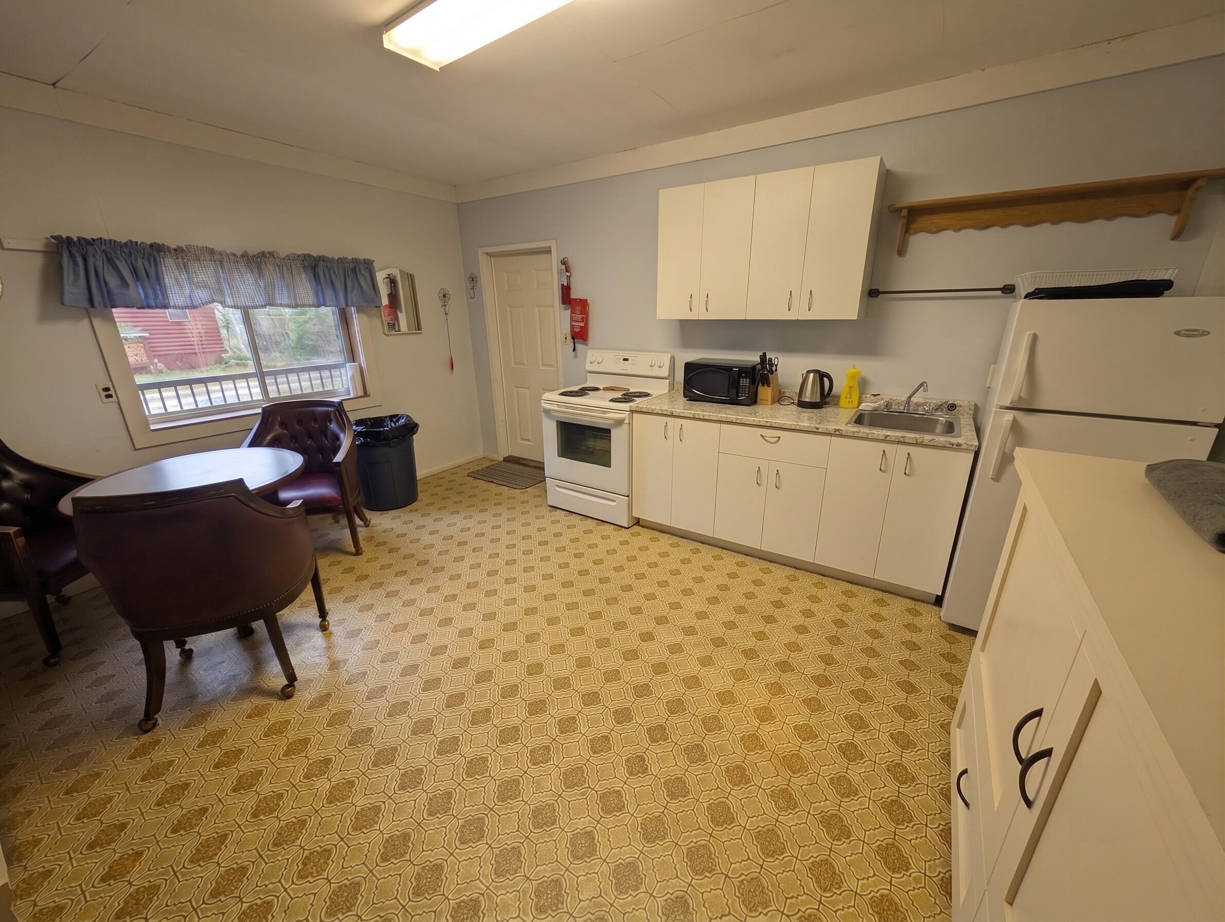 Une cuisine compacte avec des meubles blancs, une cuisinière, un four à micro-ondes et un réfrigérateur. On y trouve une table à manger avec des chaises et une fenêtre donnant sur un beau paysage.