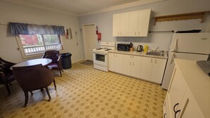 Une cuisine compacte avec des meubles blancs, une cuisinière, un four à micro-ondes et un réfrigérateur. On y trouve une table à manger avec des chaises et une fenêtre donnant sur un beau paysage.