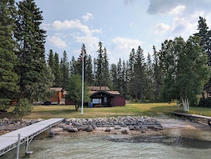 A cabin with a deck, surrounded by a forest and a small body of water.