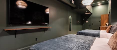 Een hotelkamer met een flatscreen televisie aan de muur, twee bedden met blauw beddengoed, een houten nachtkastje en een spiegel.