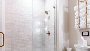 A modern bathroom with a glass-enclosed shower, a toilet, and a sink with a towel rack. - Hollyhock Suite 304: 1 Bed/1 Bath (Louisville)