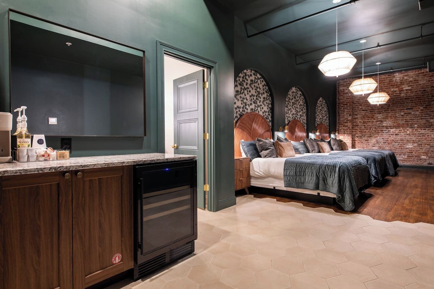 Eine moderne Küche mit dunklen Schränken und einem Geschirrspüler, ein Schlafzimmer mit einem großen Bett und einer Ziegelwand sowie ein Essbereich mit einem großen Tisch und Stühlen.