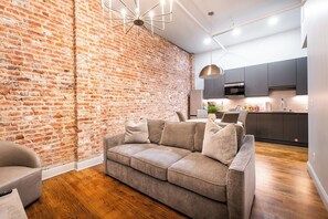 Ein modernes Wohnzimmer mit Backsteinwand, grauem Sofa und Holzboden.